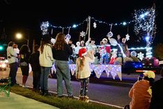 people standing in front of a float decorated with lights and snowflakes at night