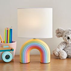 a white teddy bear sitting next to a lamp on a table with a rainbow decoration