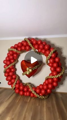 a heart - shaped balloon wreath with red balls and gold chains hanging from it's center