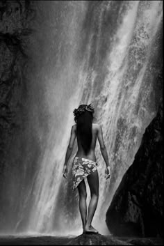 a woman standing in front of a waterfall with her back turned to the camera,