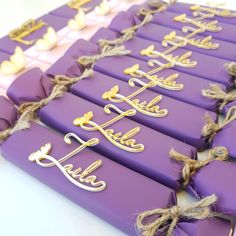 purple and gold chocolates with names on them sitting on a white counter top next to twine rope