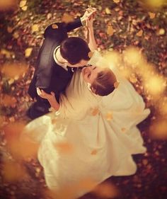 a bride and groom are dancing in the fall leaves with their arms around each other