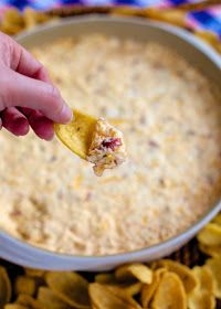 a hand holding a tortilla chip over a bowl of dip with chips on the side