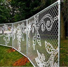 a white fence with intricate designs on the top and bottom part, in front of some trees