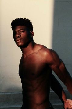 a shirtless man holding a tennis racquet in front of a white wall