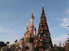 a large christmas tree in front of a castle at disneyland world with people standing around it