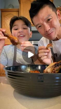 a father and son eating chicken in the kitchen