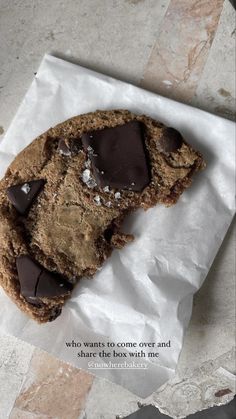 a cookie with chocolate chips on it sitting on top of a piece of paper that says, who wants to come over and share the box with me?