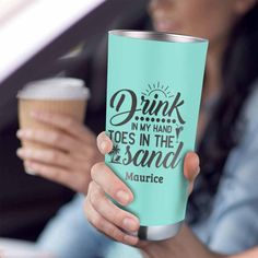 a woman holding a cup with the words drink in my hand toes in the sand