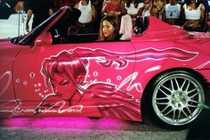 a woman sitting in the driver's seat of a pink car with graffiti on it