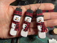 three snowmen wearing hats and scarfs are hanging from the palm of a person's hand