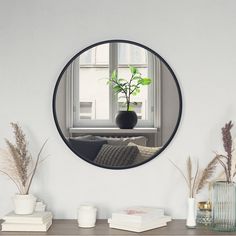 a round mirror on the wall above a table with vases and plants in front of it