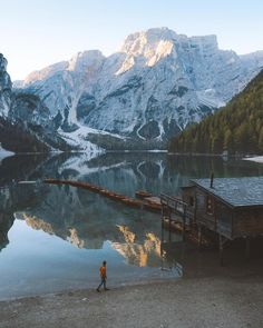 a person standing on the shore of a lake with mountains in the background and a dock