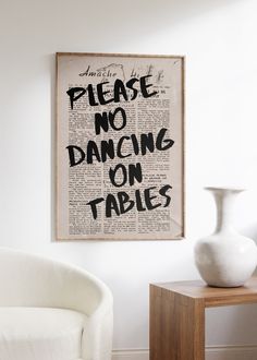 a white chair sitting next to a table with a vase on it and a sign that says please no dancing on tables