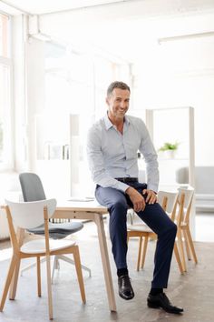 a man sitting on top of a wooden chair next to a white table and chairs