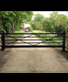 an open gate leading to a dirt road with trees on both sides and a house in the distance