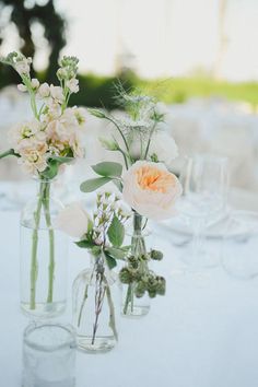 two vases with flowers are sitting on a table in front of wineglasses