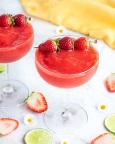 two margaritas with strawberries and lime garnish sit on a marble table