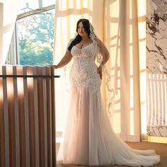 a woman standing in front of a window wearing a wedding dress with sheer lace and beading