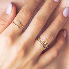 a woman's hand with two gold rings on her fingers and the word love spelled in small letters