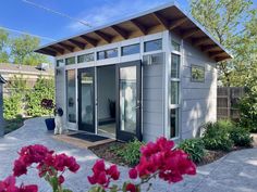 a small gray building sitting in the middle of a yard with pink flowers around it