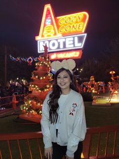 a woman standing in front of a motel sign at night with lights on the trees