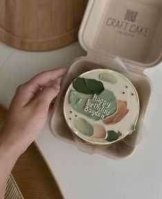 a person is holding a birthday cake in a box on a table with other items