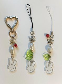 three key chains with charms attached to them on a white surface, one has a heart and the other is a bunny