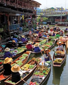 many boats filled with people and vegetables floating down a river in the middle of a city