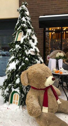 a large teddy bear sitting next to a small christmas tree in front of a building