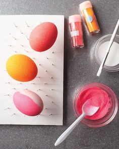 an assortment of paints and brushes on a table next to a paper with three eggs in it