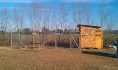 an outhouse in the middle of a field next to a fence and some trees