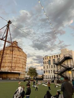 people are standing in the grass near a grain silo and building with lights strung above it