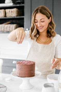 a woman decorating a chocolate cake with pink sprinkles on the top