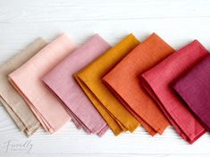 six different colors of linens laid out on a white wooden surface with one folded in half