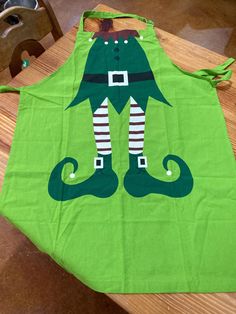 a green apron with an elf's legs on it sitting on top of a wooden table