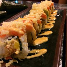 sushi rolls with sauce drizzled on them sitting on a black plate