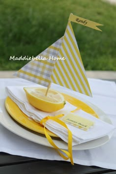 a yellow and white plate topped with a lemon slice next to a small sail boat