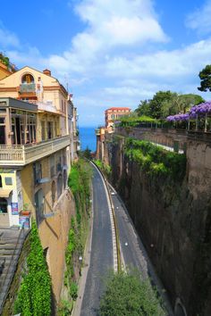 an empty street with buildings on both sides and the ocean in the background