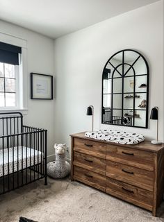 a baby's room with a crib, dresser and mirror on the wall