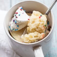 a cup filled with white frosting and sprinkles next to a spoon