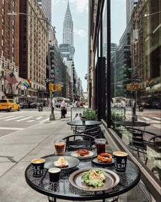 a table with plates of food on it sitting in front of a window overlooking a city street