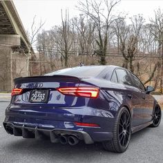 the rear end of a blue car parked in a parking lot next to a bridge