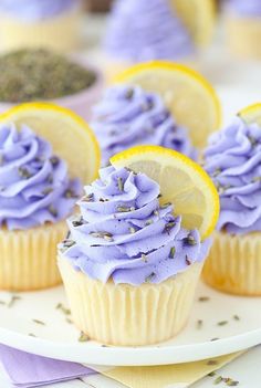 cupcakes with purple frosting and lemon slices on a white plate next to lavender sprinkles