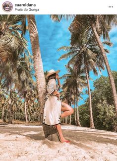 a woman sitting on top of a palm tree next to the ocean with her legs crossed