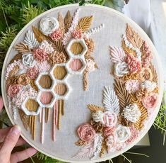 someone is holding up a embroidery project with flowers and leaves on the front of it