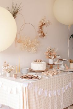 a table topped with cake and desserts on top of a white table covered in balloons