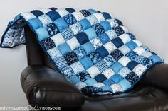 a blue and white patchwork blanket sitting on top of a black leather chair next to a wall