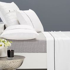 a bed with white sheets and pillows next to a vase filled with flowers on a table