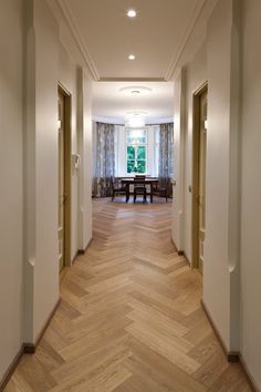 an empty hallway leading to a dining room and living room with wood flooring on both sides